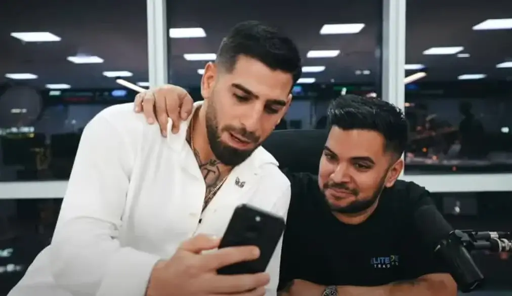 Pako Thawani mostrando sus resultados de trading en el móvil al campeón de la UFC Ilia Topuria en una oficina de trading de alta tecnología, ambos celebrando el éxito.