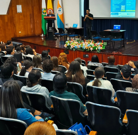 "Orador presentando estrategias de negocios digitales y marketing de afiliación ante una audiencia en un auditorio lleno, mostrando proyecciones de ventas en pantalla gigante."
