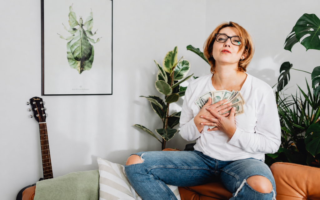 mujer-ahorrando-dinero-finanzas-personales-vida-real.png Mujer sentada en casa sujetando dinero como símbolo de ahorro, control económico y finanzas personales bien gestionadas