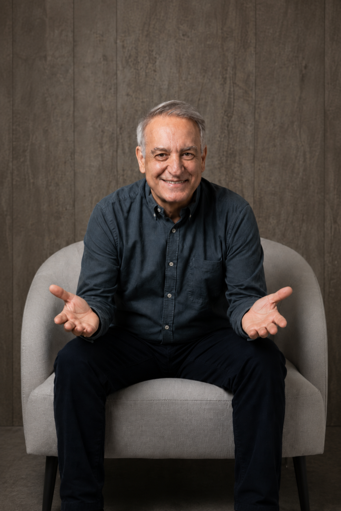 curso-finanzas-personales-vida-real-economista-brazos-abiertos.webp Economista sentado con los brazos abiertos y las palmas hacia arriba, imagen representativa de un curso de finanzas personales para la vida real.
